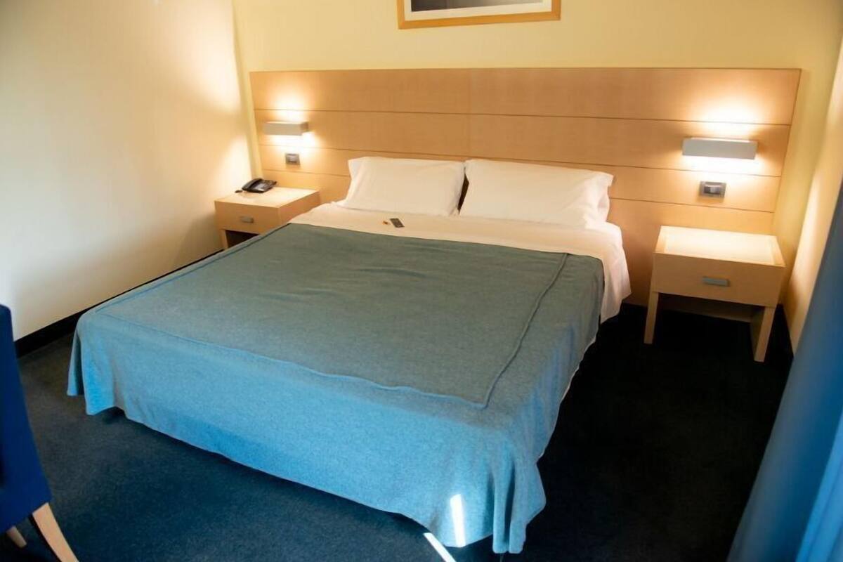 A hotel room with a bed, bedside tables, a nightstand, and a wall-mounted lamp.