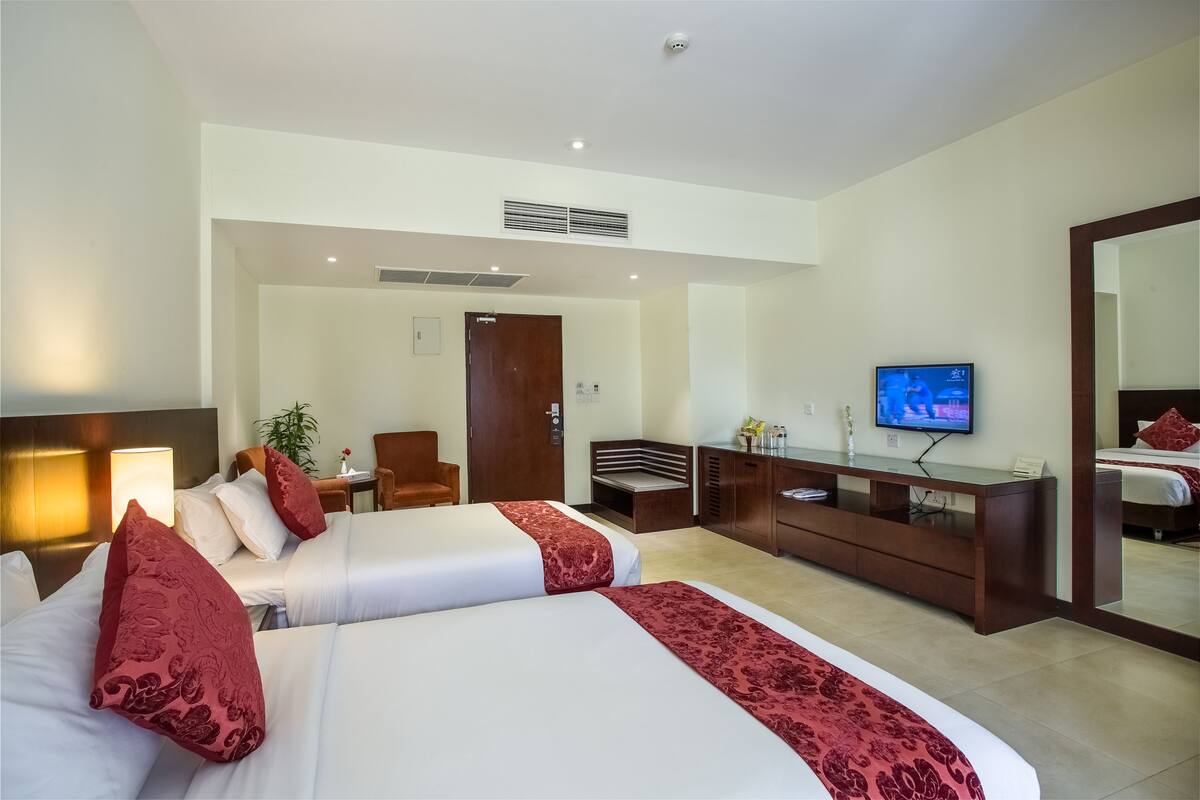 Una habitación de hotel con dos camas, televisión, escritorio y espejo.