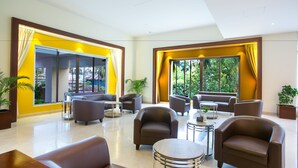 Un hall amplio con varias zonas de estar, ventanas grandes con cortinas y plantas de interior.
