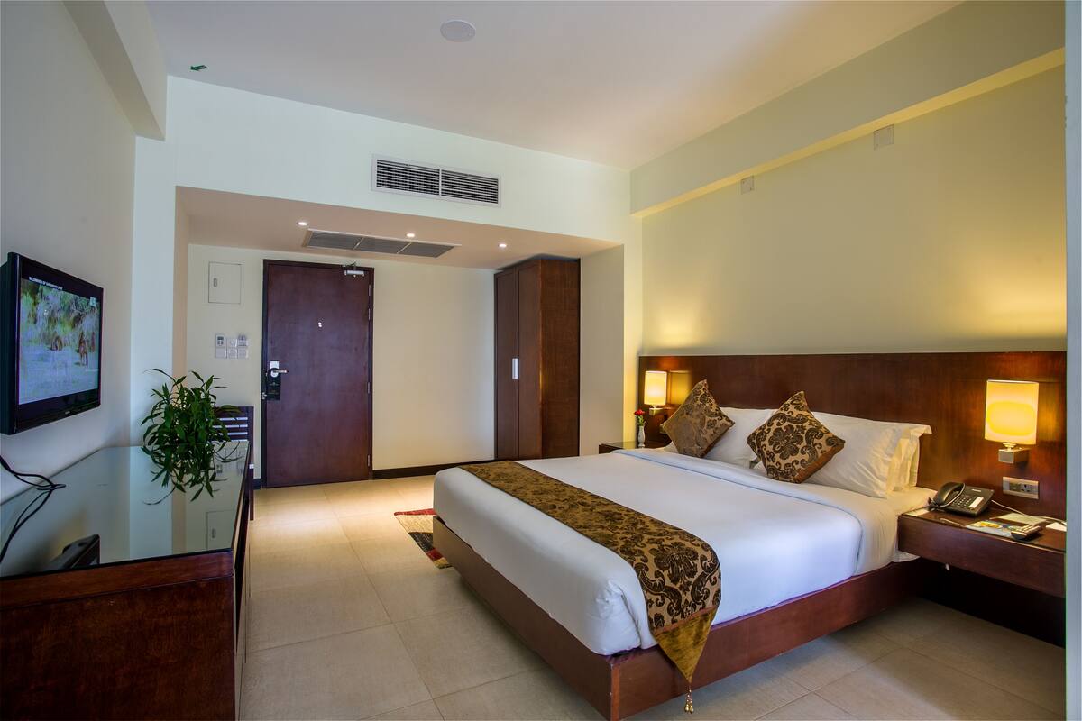 Habitación de hotel con una cama grande, lámparas de noche, un escritorio con ordenador y una televisión en la pared.