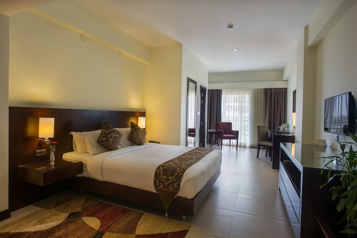 Una habitación de hotel con una cama grande, mesitas de noche, televisión, escritorio y una silla.
