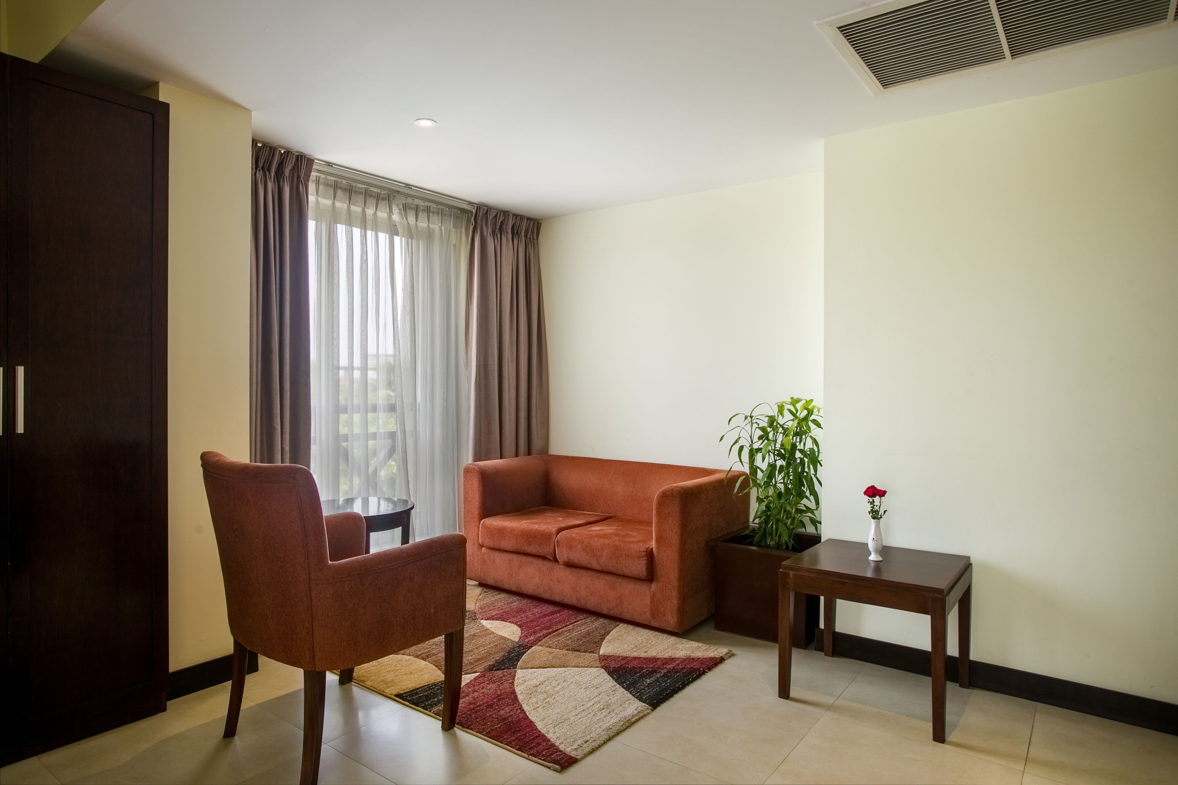 A living room with a sofa, armchair, and a small table with a plant and vase.