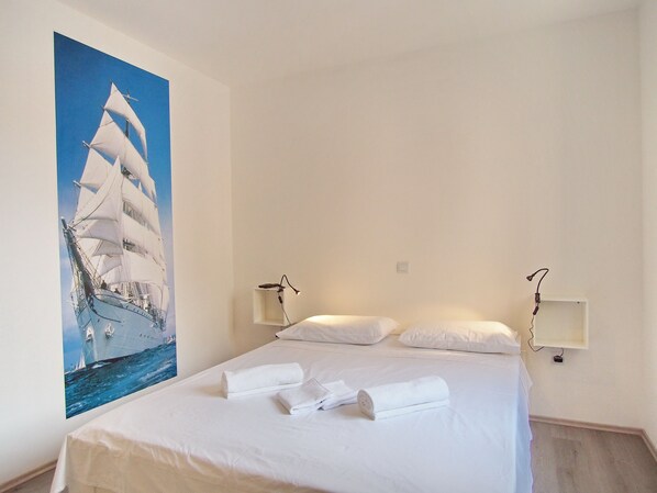 A hotel room with a large bed, two bedside tables, a wall-mounted lamp, and a painting of a sailing ship. - Icy-House (Dubrovnik)