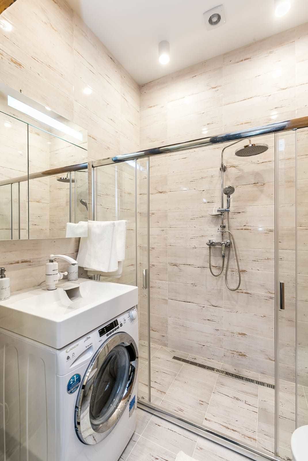 Un baño moderno con ducha envuelta en vidrio, lavadora integrada y un espejo grande.