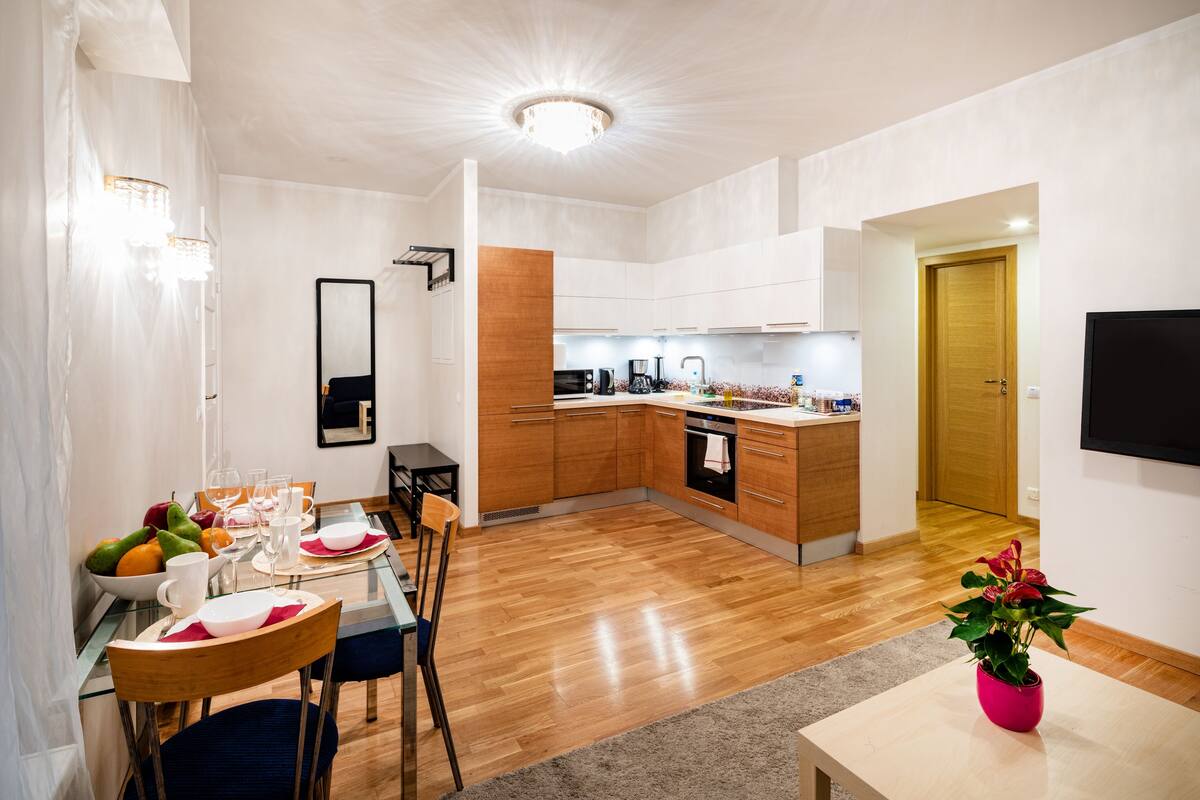 A modern kitchen with wooden cabinets, a dining area with a glass table, and a potted plant.