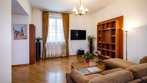 A living room with a sofa, a coffee table, a bookshelf, a TV, and a chandelier. - Old Riga Apartments (Riga)