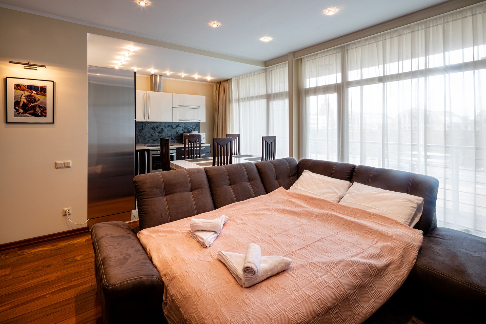 A modern hotel room with a large bed, a dining area, and a kitchen.