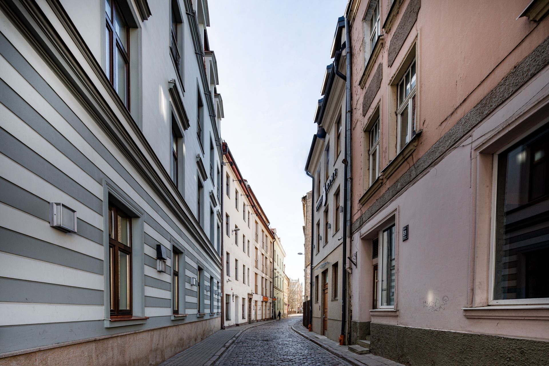 A narrow cobblestone street flanked by historic buildings with large windows and traditional facades.