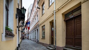 A narrow cobblestone street flanked by buildings with traditional European architecture, including a large wooden door and a metal lamp post. - Old Riga Apartments (Riga)