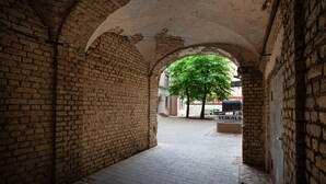 An arched brick corridor with a tree in the center, leading to a building labeled "VEIKALS." - Old Riga Apartments (Riga)