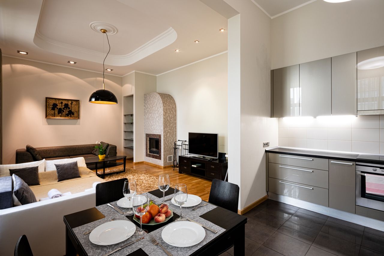 A modern living room with a sofa, dining table, and kitchen area with cabinets and a TV.