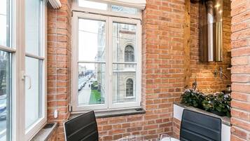 Ein Eckzimmer mit Backsteinwand, einem Fenster mit Blick auf eine Straße, einem kleinen Waschbecken und einem Tisch mit Stühlen.