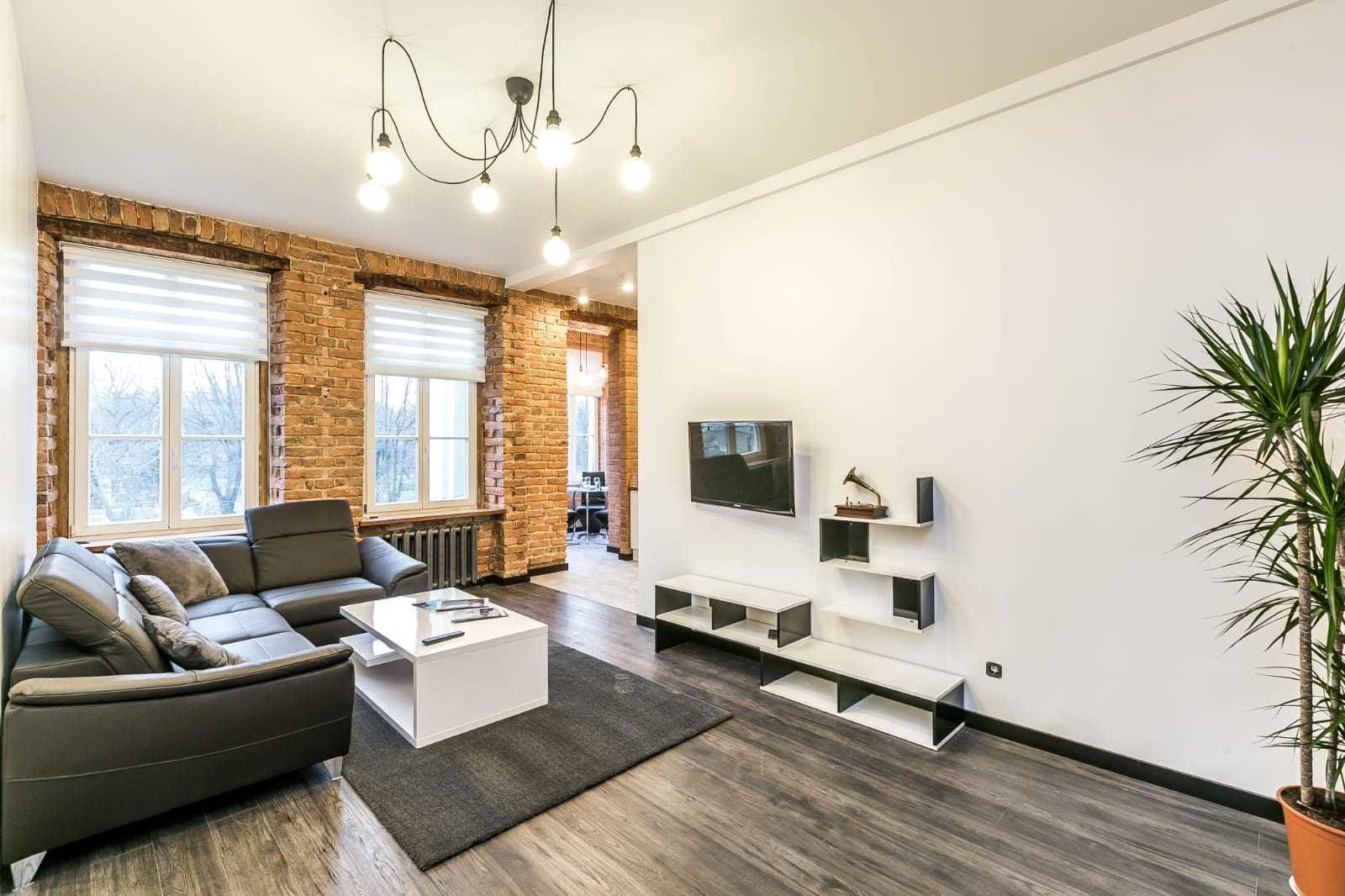 A modern living room with a brick wall, a sofa, a coffee table, a TV, and a plant.