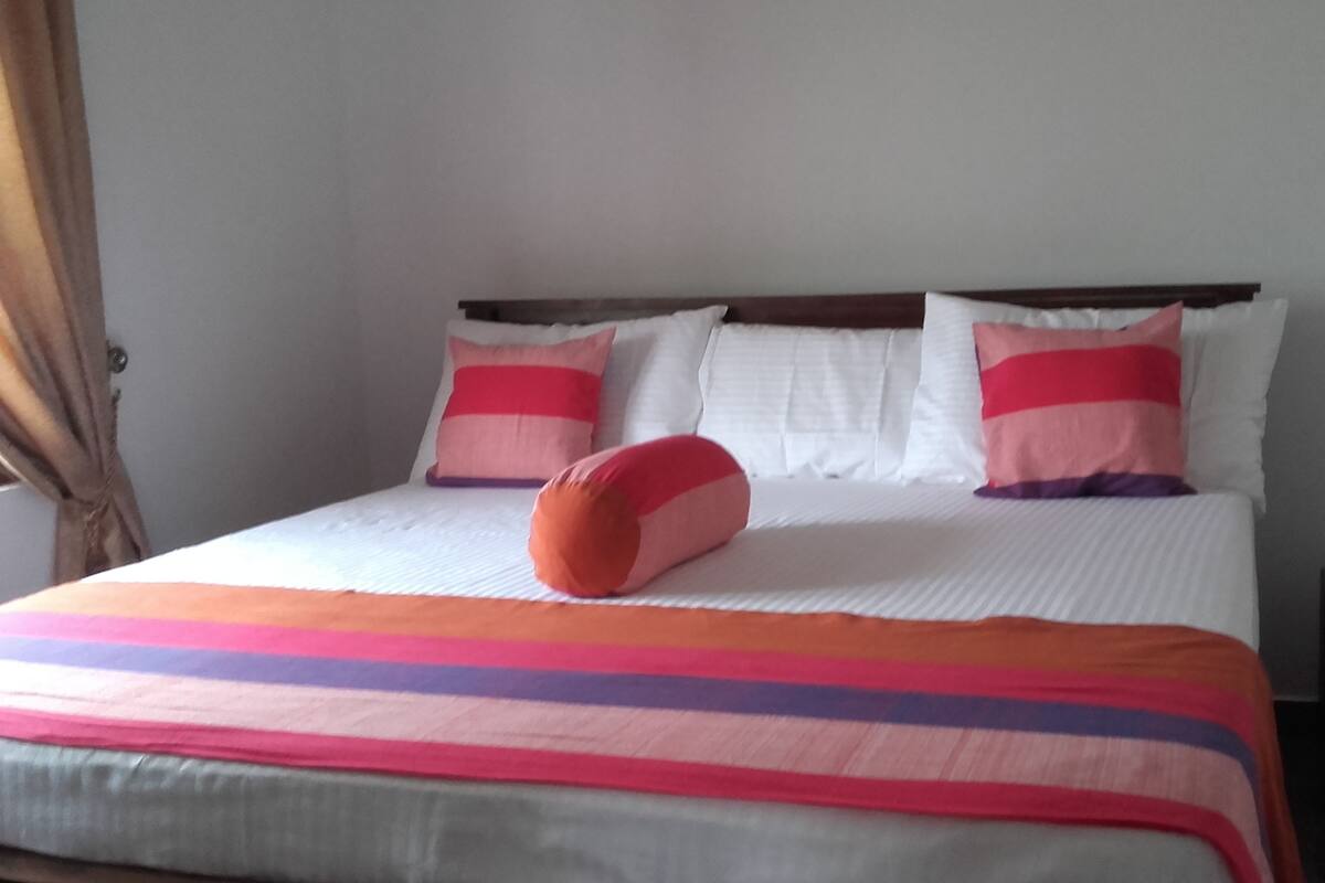 A bed with a colorful striped blanket and two pillows with pink and red stripes.