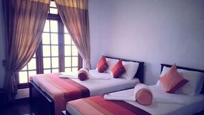 A hotel room with two beds, each with a white mattress and red and orange pillows. The room has a window with curtains and a view of the outside. - The European Gate (Anuradhapura)