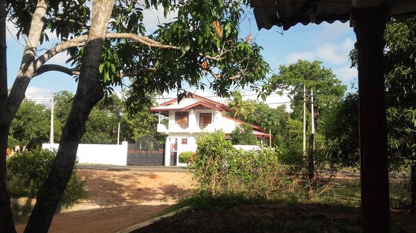 A two-story house with a red roof, surrounded by greenery and a white fence.