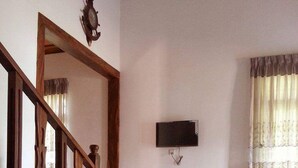 A living room with a wooden staircase, a flat-screen TV mounted on the wall, and a beige sofa. - The European Gate (Anuradhapura)