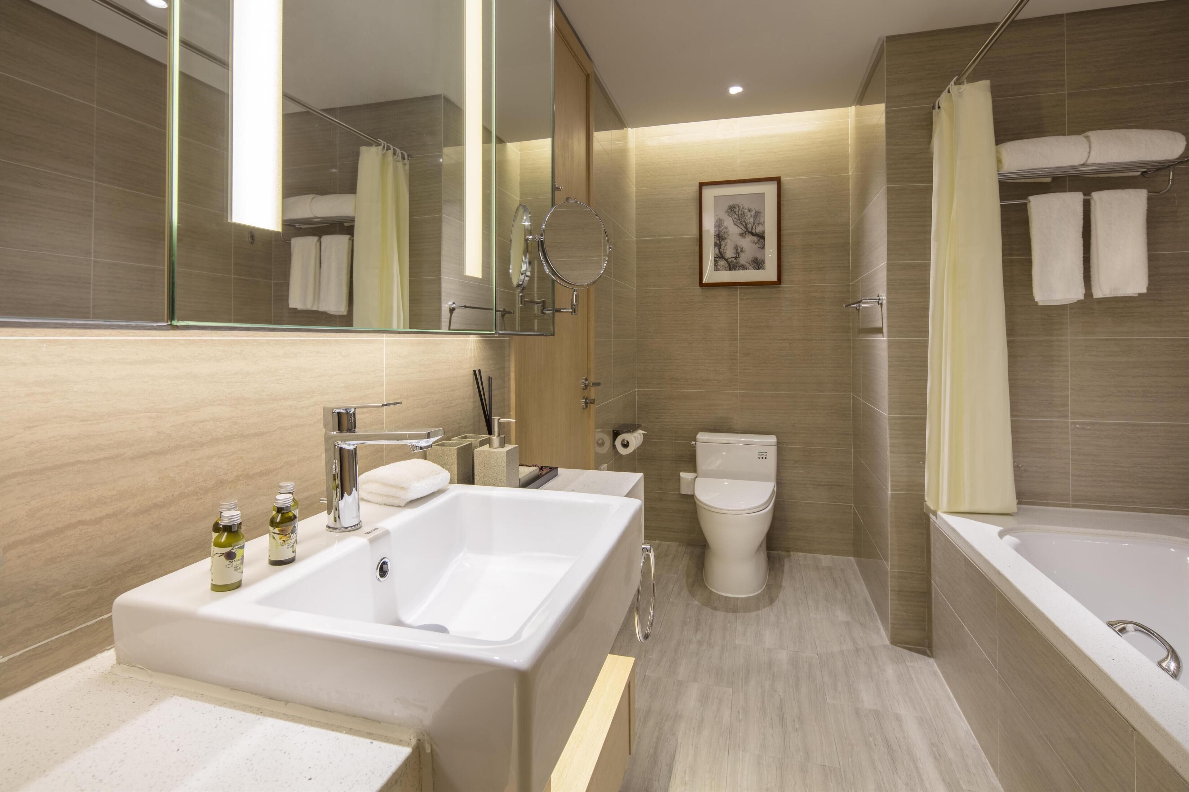 A modern bathroom with a large white bathtub, a separate shower area, and a toilet. There are two sinks with mirrors, and a framed picture hangs on the wall.