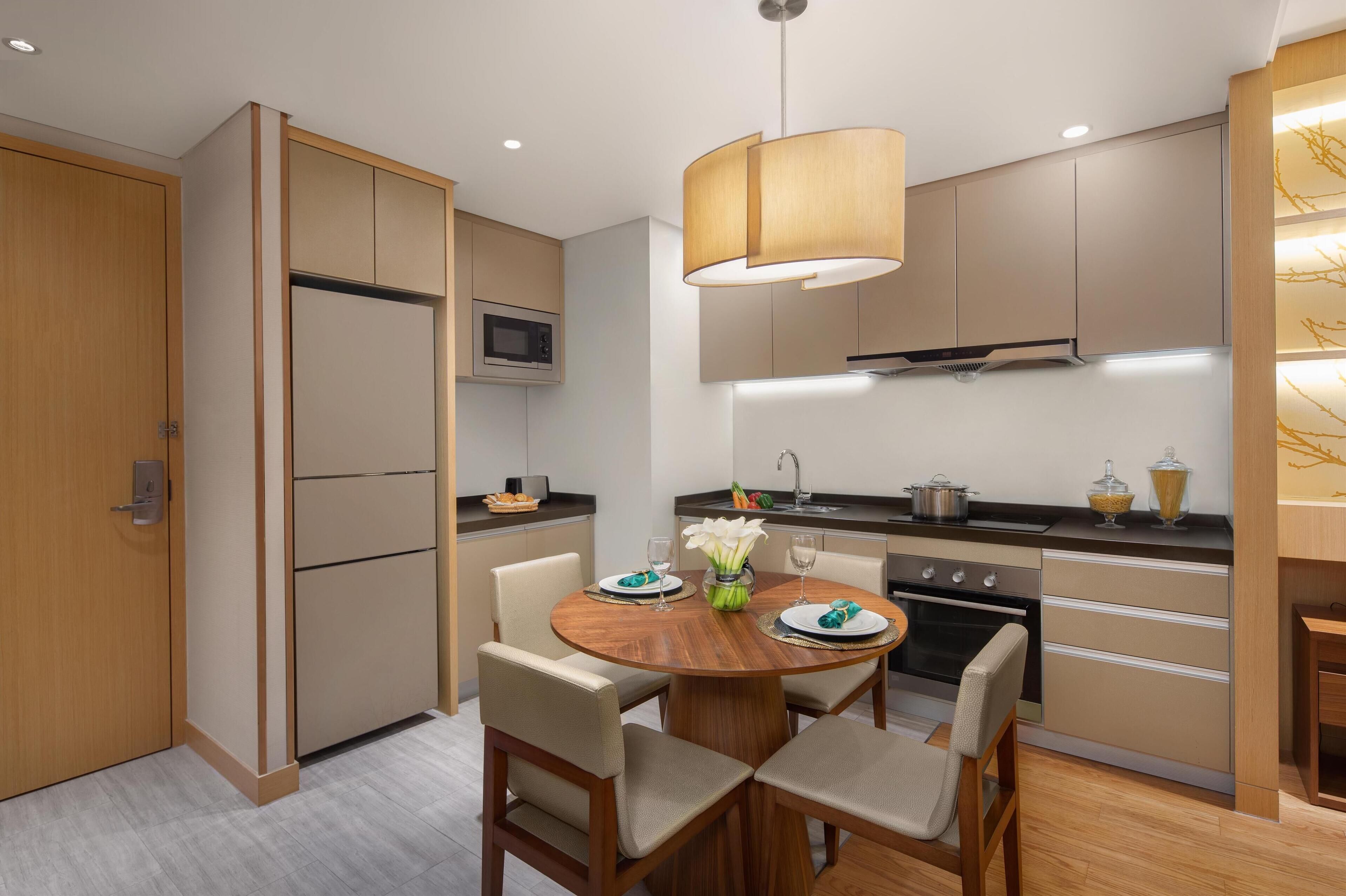 Una cocina moderna con zona de comedor, que incluye una mesa de madera, sillas, una lámpara colgante y electrodomésticos empotrados.