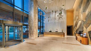 A modern hotel lobby with a reception desk, large windows, and decorative hanging elements. - Somerset Baitang Suzhou (Suzhou)