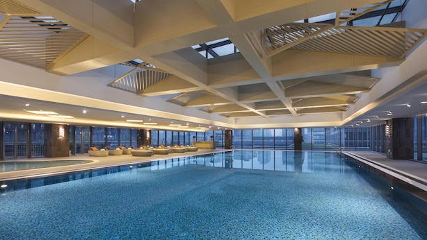 A large indoor swimming pool with a modern design, featuring a high ceiling with skylights and a clear view of the cityscape through large windows. - Somerset Baitang Suzhou (Suzhou)