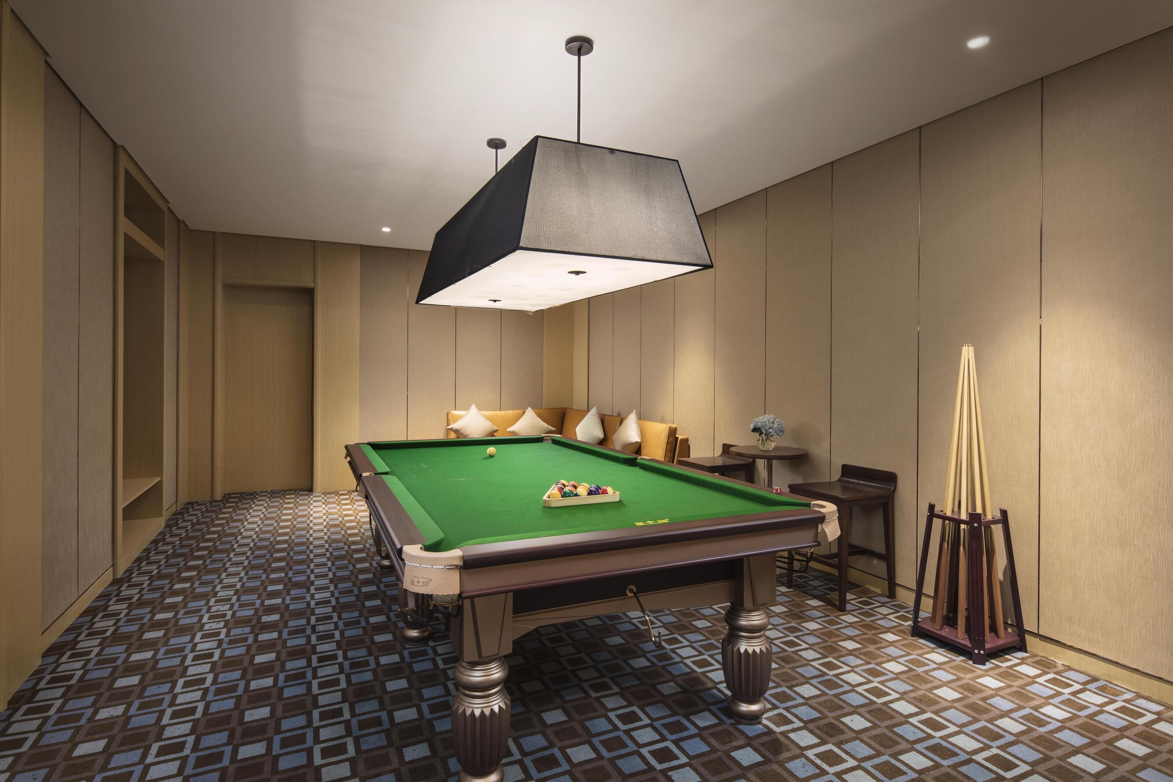 A pool table in a room with a patterned floor, a hanging light fixture, and a small table with chairs.