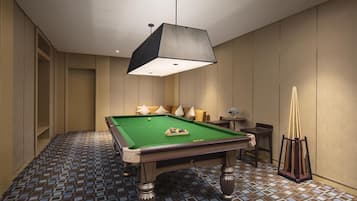 A pool table in a room with a patterned floor, a hanging light fixture, and a small table with chairs.