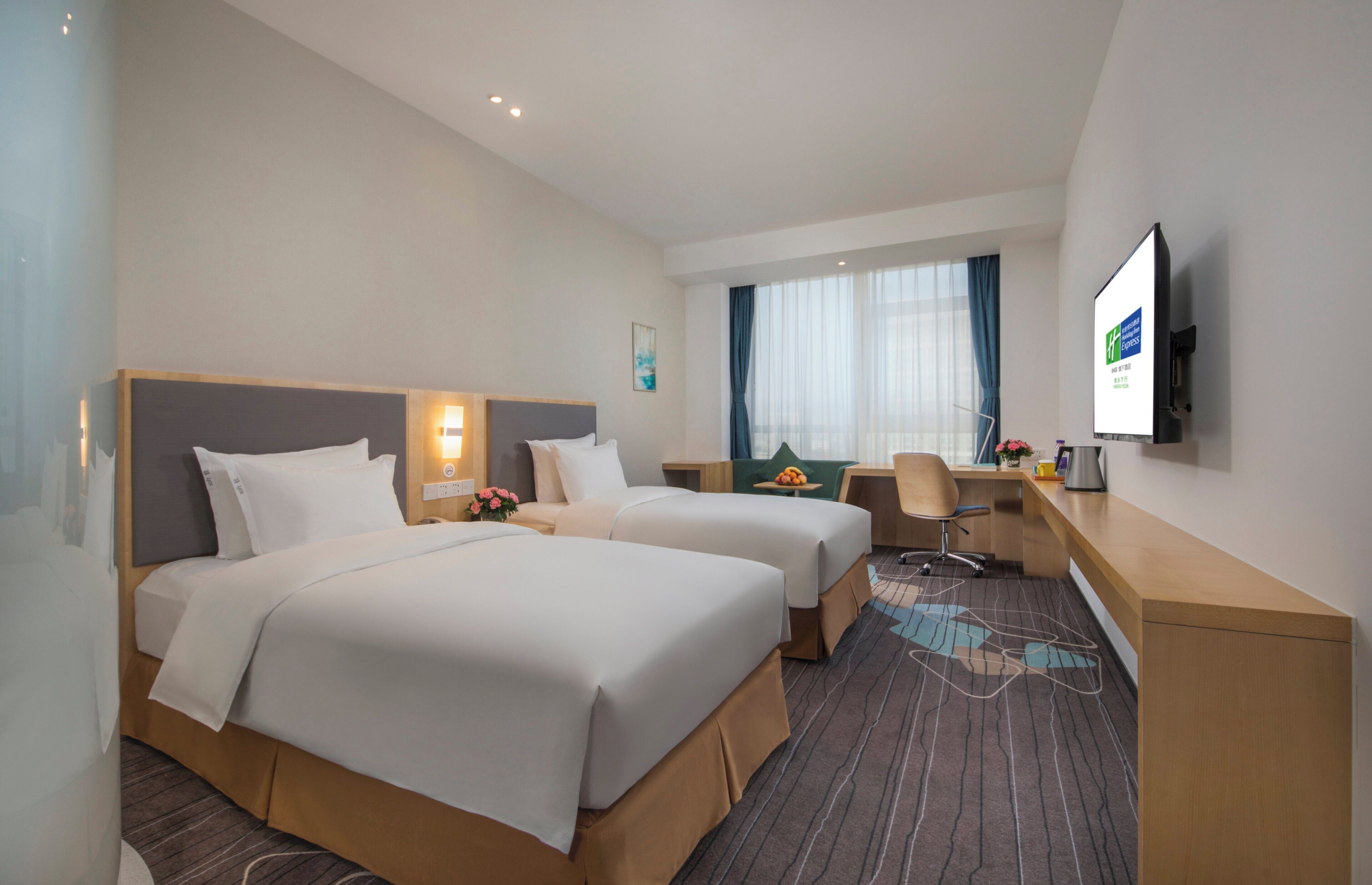 A hotel room with two beds, a desk, a chair, a television, and a window with curtains.