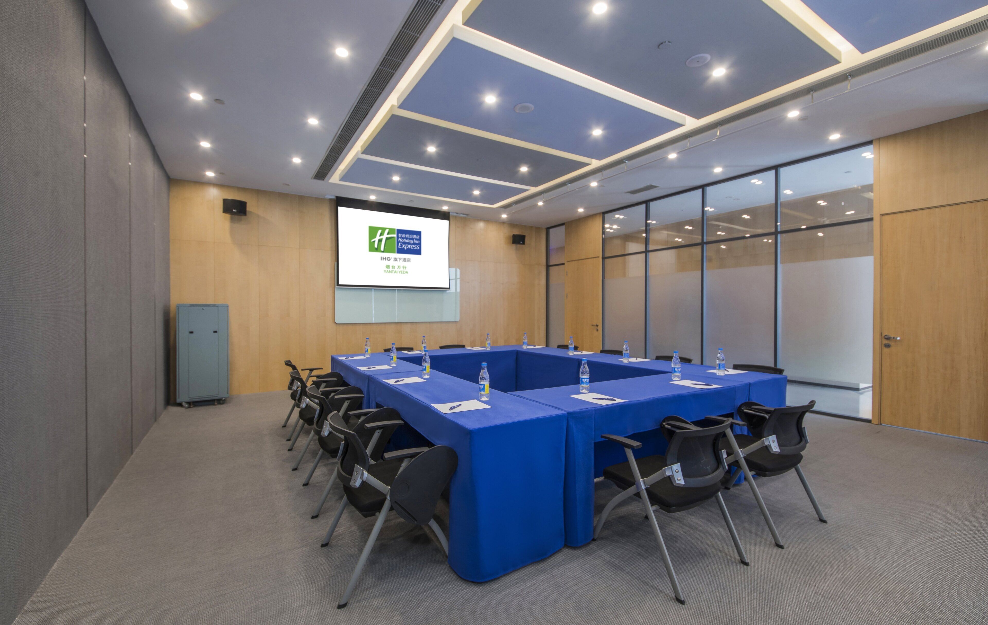 Una sala conferenze con un lungo tavolo, sedie, uno schermo per proiettore e un armadietto in legno.