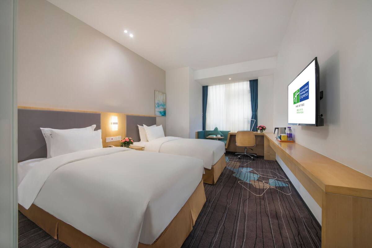 A hotel room with two beds, a desk, a chair, a TV, and a window with curtains.