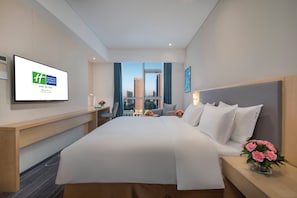 A hotel room with a bed, a desk, a chair, a TV screen, and a view of the cityscape. - Holiday Inn Express Yantai Yeda by IHG (Yantai)