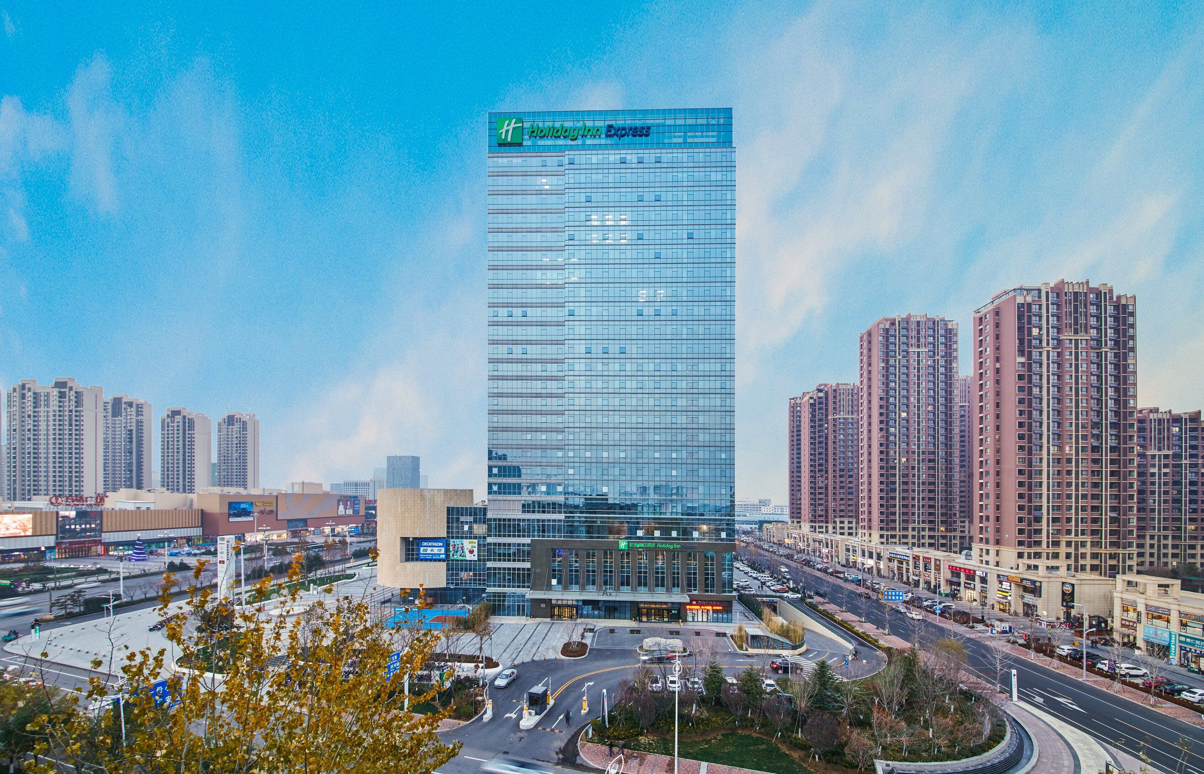 A modern hotel with a glass facade, surrounded by high-rise buildings and a busy urban street.