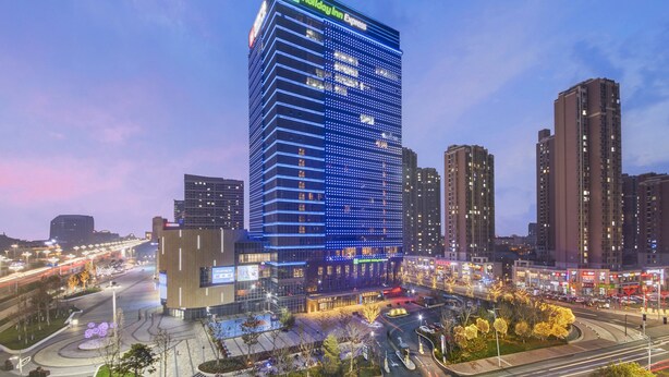A high-rise Holiday Inn Express hotel with a modern glass facade, surrounded by a busy urban street and other high-rise buildings. - Holiday Inn Express Yantai Yeda by IHG (Yantai)