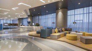 A spacious lobby with a modern design, featuring a reception desk, seating area with sofas and ottomans, and large windows with sheer curtains. - Holiday Inn Express Yantai Yeda by IHG (Yantai)