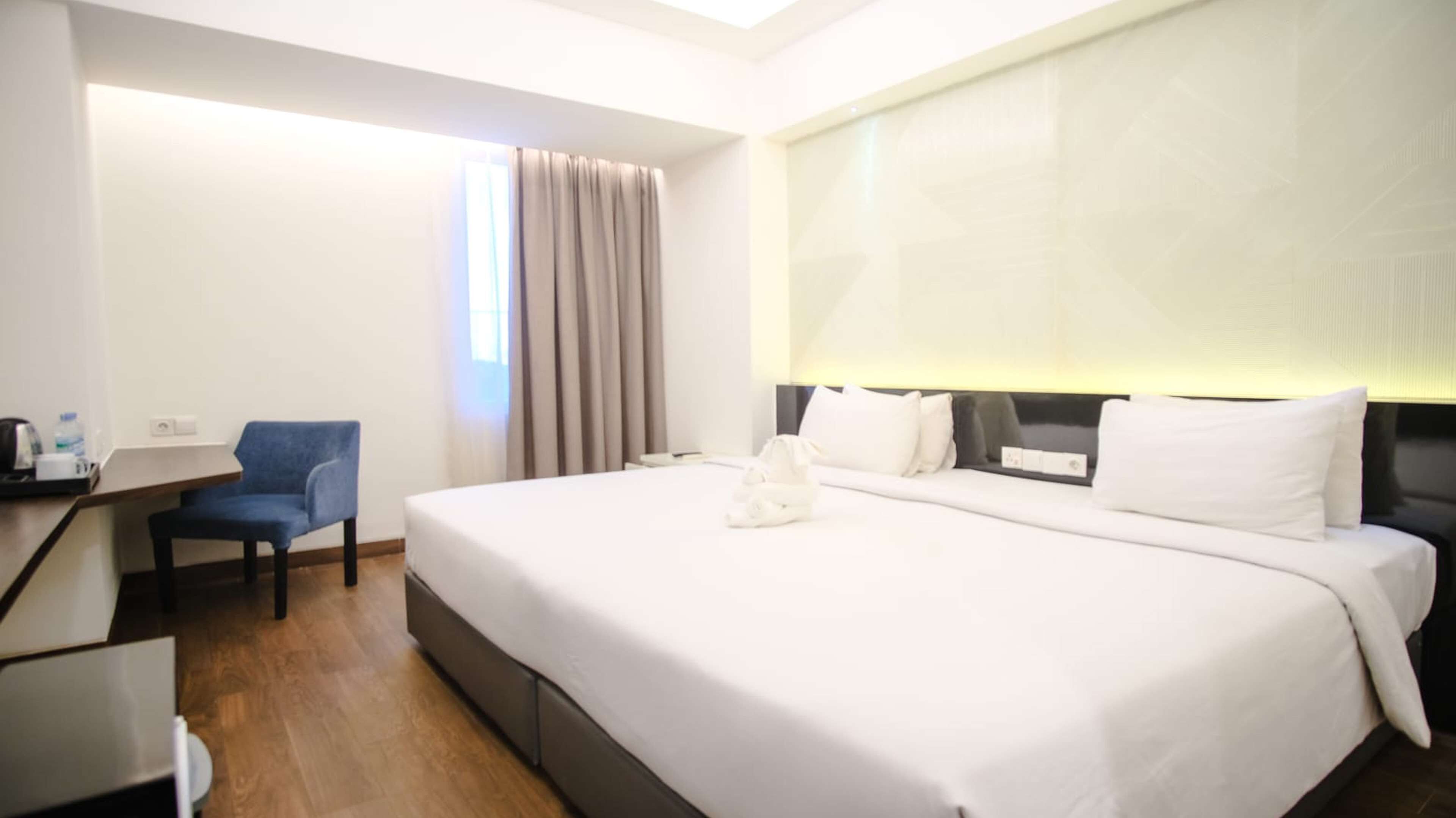 Une chambre d’hôtel avec un grand lit, un bureau avec une chaise, une fenêtre avec des rideaux et une table de chevet avec une lampe.