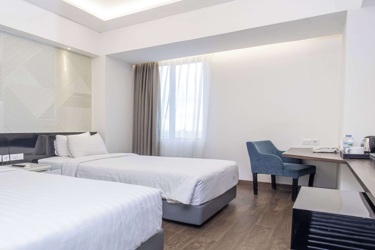 A hotel room with two beds, a desk, a chair, and a large window with curtains.
