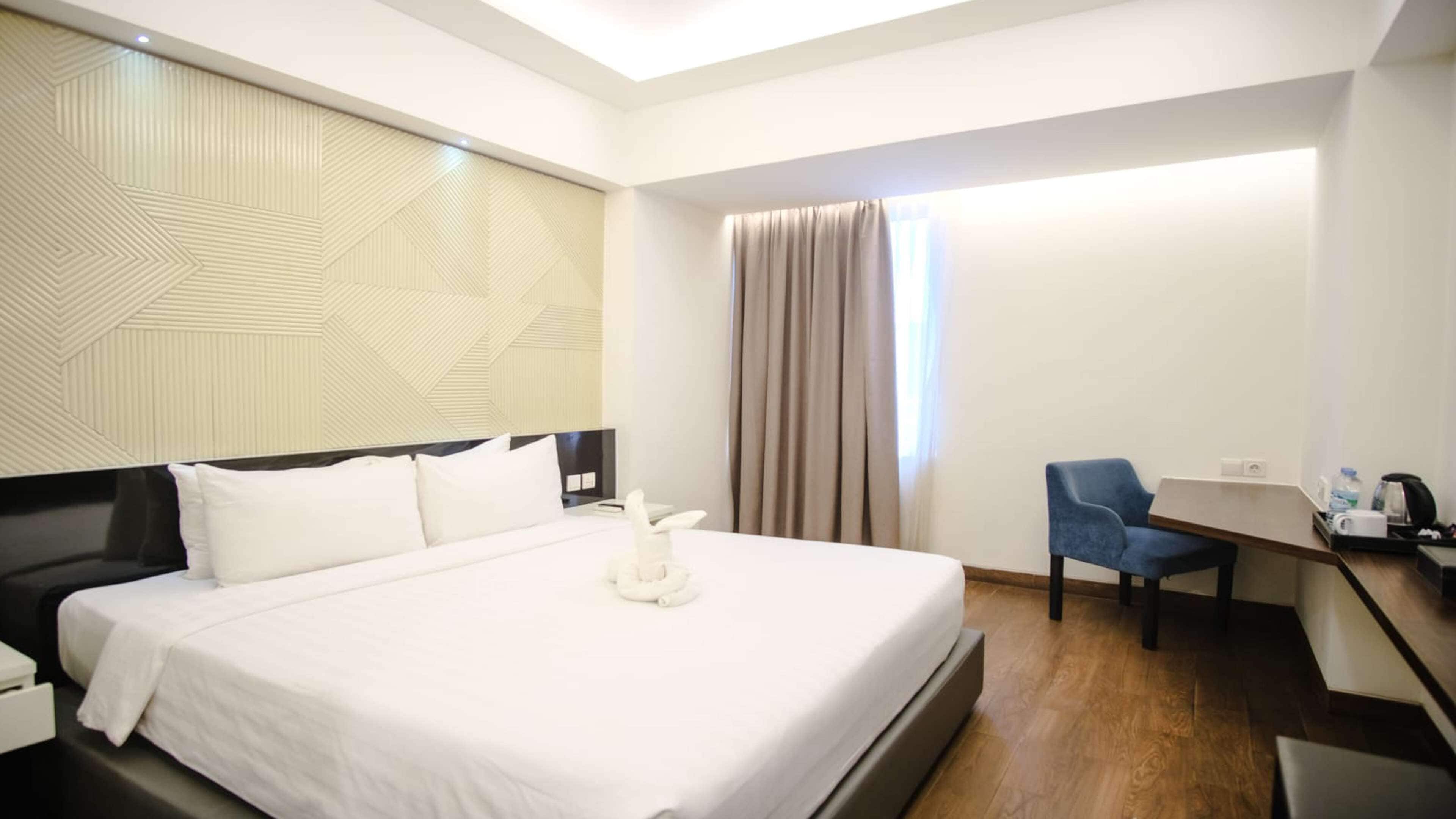 Une chambre d’hôtel avec un grand lit, un bureau, une chaise et une fenêtre avec des rideaux.