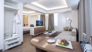 A modern hotel room with a bed, a desk, a sofa, and a dining table with fruit. - Golden Tulip Essential Makassar (Makassar)