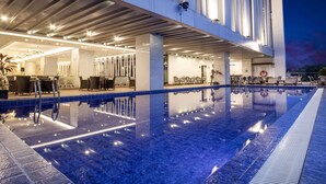 A modern hotel pool area with a clear pool, lounge chairs, and a covered seating area. - Golden Tulip Essential Makassar (Makassar)