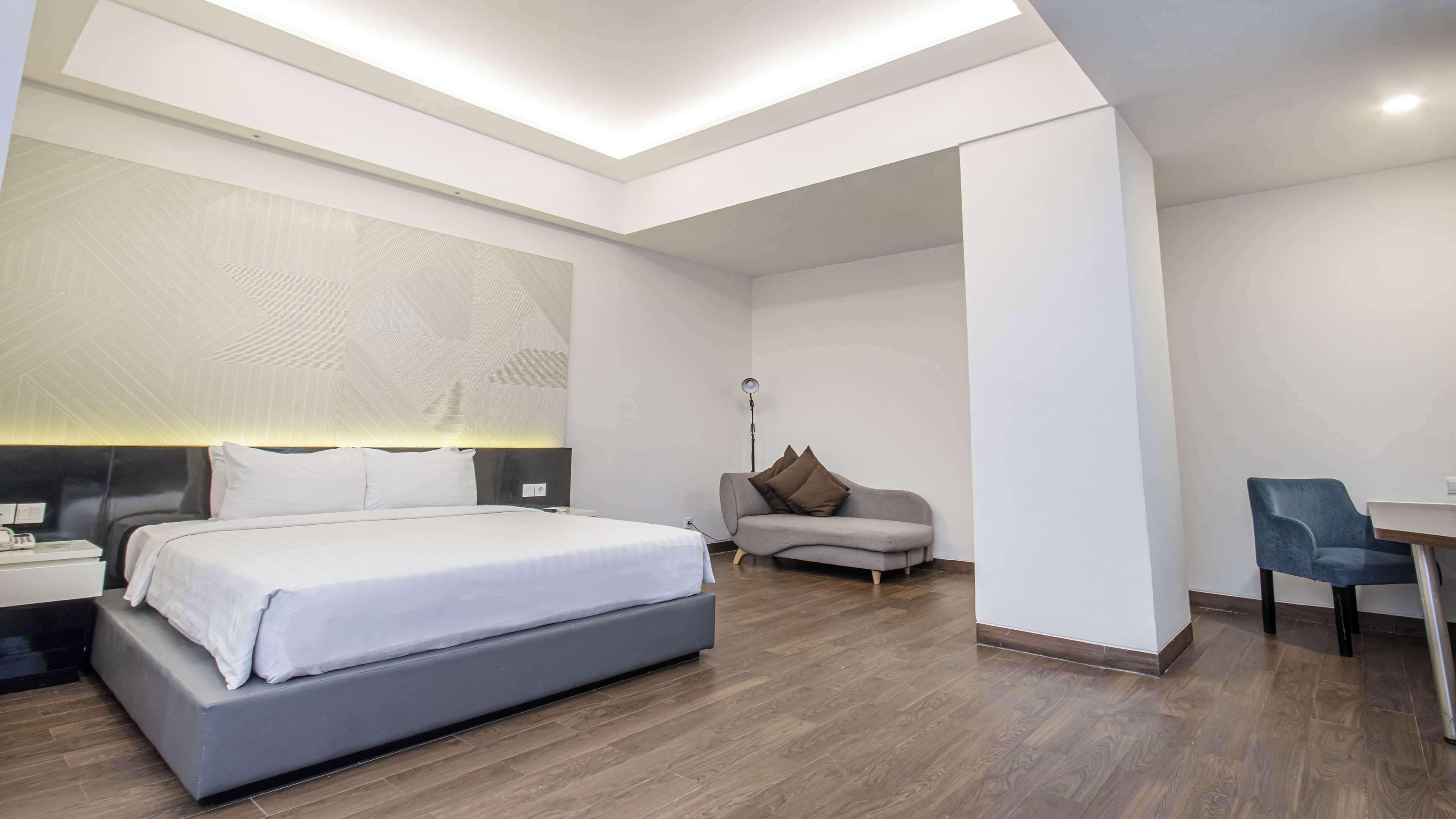 A modern hotel room with a large bed, a sofa, a desk, and a floor lamp.