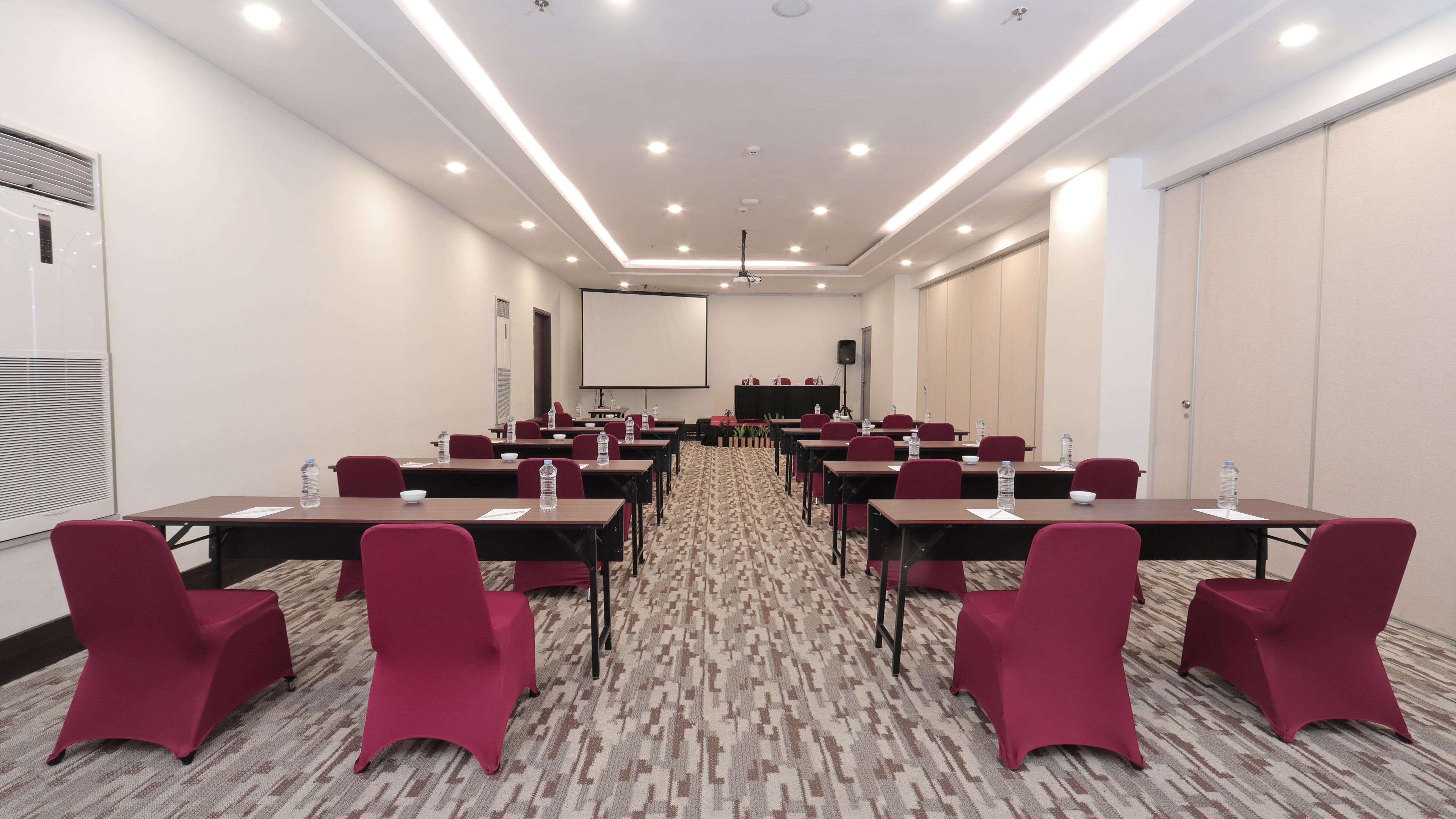 A conference room with tables and chairs, a projector screen, and a carpeted floor.