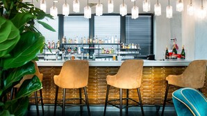A bar area with a counter, multiple bottles, and three chairs. - Kopster Hotel Lyon Groupama Stadium (Decines-Charpieu)