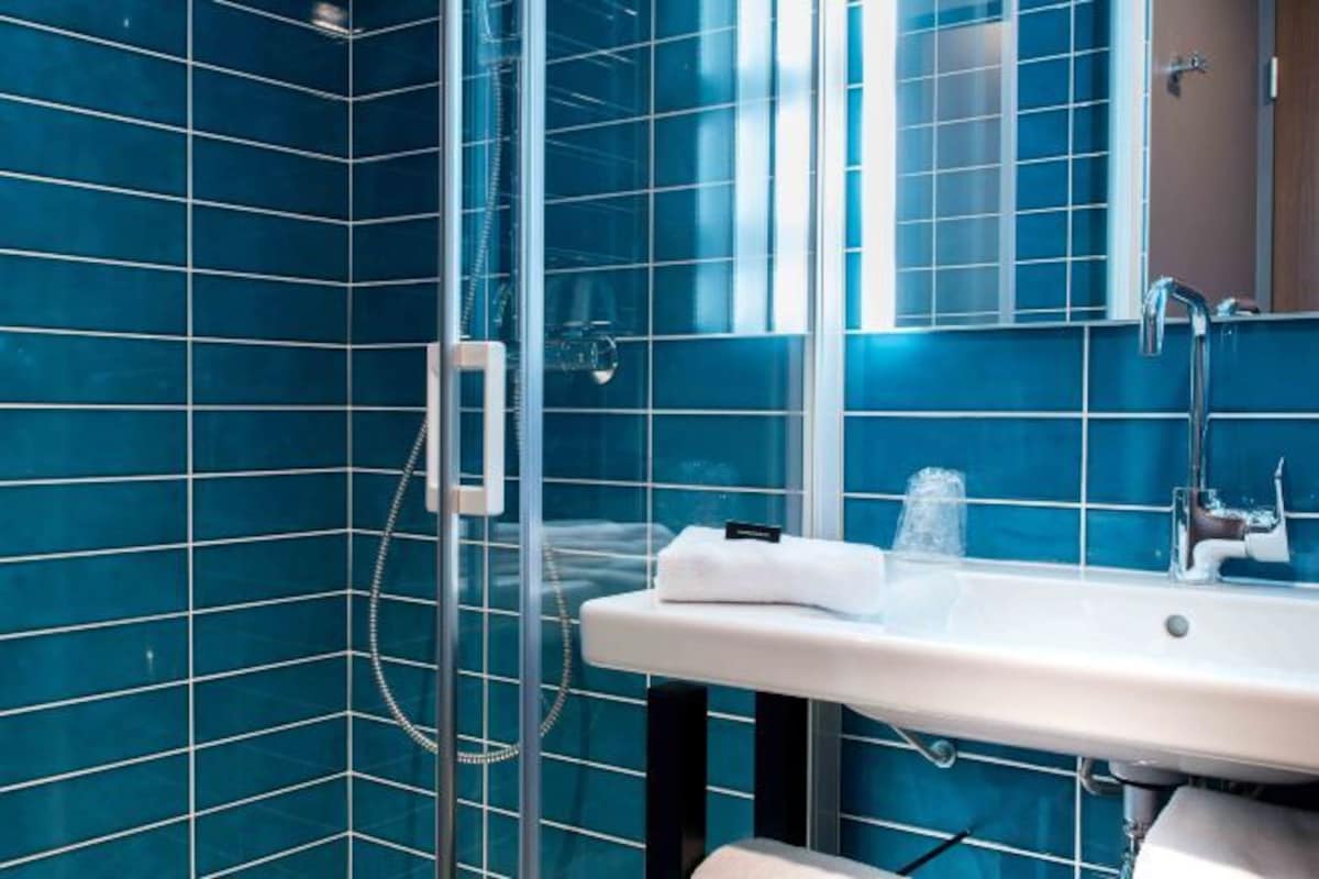 A bathroom with blue-tiled walls, a glass shower enclosure, a white sink, and a mirror.