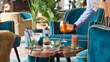 Un espace bar avec une table ronde en bois, plusieurs boissons et des chaises recouvertes d’un tissu de couleur turquoise.
