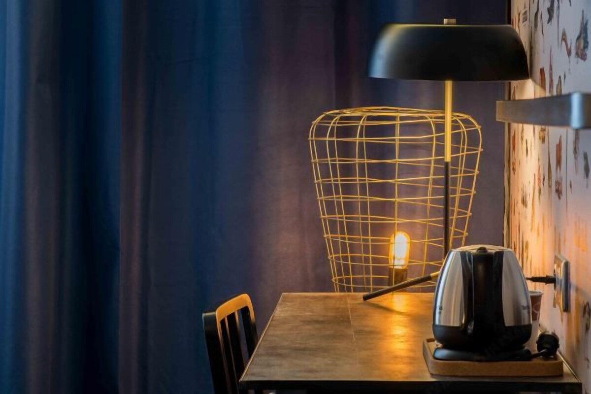 A table with a kettle and a lamp with a wireframe shade.