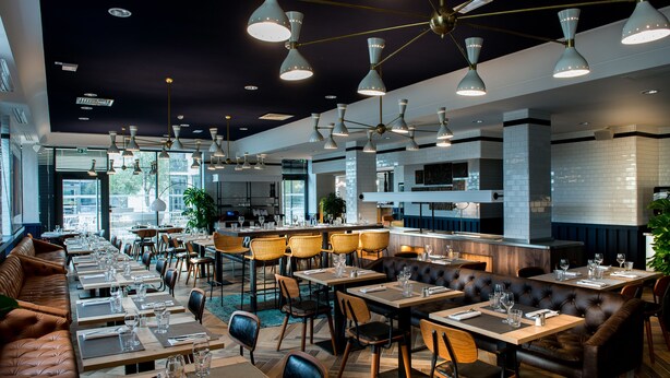 A restaurant with multiple dining areas, including booths and tables, and a bar area. - Kopster Hotel Lyon Groupama Stadium (Decines-Charpieu)