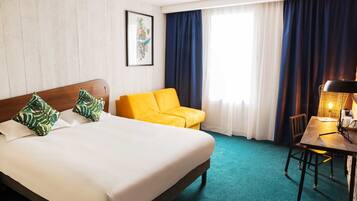 Una habitación de hotel con una cama, un sofá amarillo, un escritorio con lámpara y una ventana con cortinas.