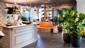 A modern reception area with a central desk, seating, and a bookshelf. - Kopster Hotel Lyon Groupama Stadium (Decines-Charpieu)