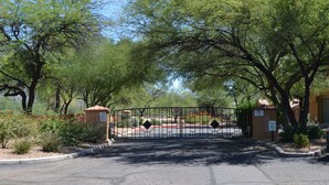 A gated entrance with a metal gate, surrounded by trees and a small building.