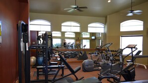 A gym with various exercise equipment, large windows, and a ceiling fan.